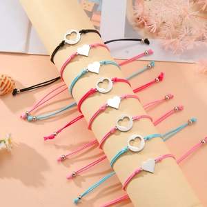 Detalle de ocho pulseras ajustables con dijes de corazón en un soporte beige