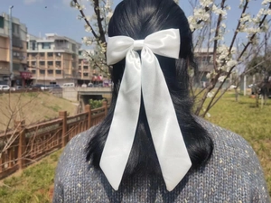 Rear view of a large white satin bow hair clip with long ribbons on black straight hair