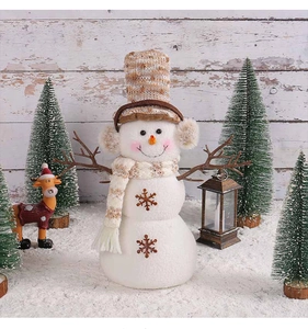 Close-up of plush Christmas snowman with knitted hat and snowflake details in snow scene