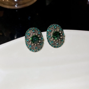 Macro detail of vintage oval earrings with green gemstone and blue rhinestones inlay