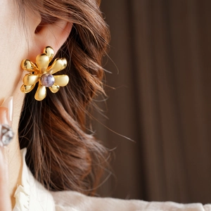 Close-up of a model wearing 18k gold-plated flower earrings with a purple pearl center