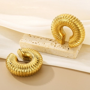 Detail goldener hohler C-förmiger Ohrringe mit vertikalen Streifen auf einem Steinständer