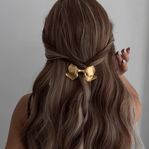 Elegant gold bow hair clip styled on wavy brown hair for a sophisticated ponytail look