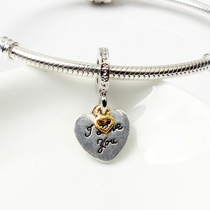 Macro shot of silver heart charm with 'I Love You' engraving and gold hollow heart