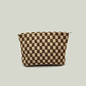 Detail of a brown and beige checkerboard knit makeup bag with top zipper and trapezoid shape