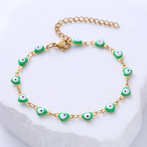 Detail of gold chain bracelet with eleven green heart-shaped evil eye charms on a stone base
