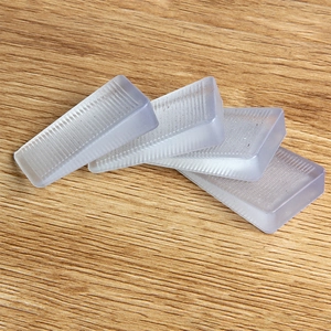 Four transparent plastic leveling wedges with anti-slip ridges on a light wood surface