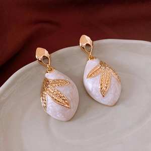 Macro detail of gold leaf pattern on white marble teardrop earrings on velvet