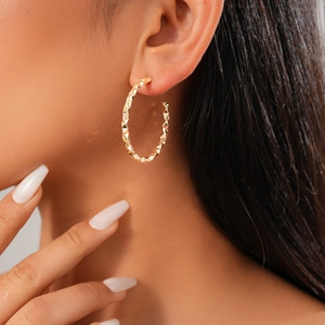 Close-up of model wearing a textured golden geometric C-shaped earring with metallic finish
