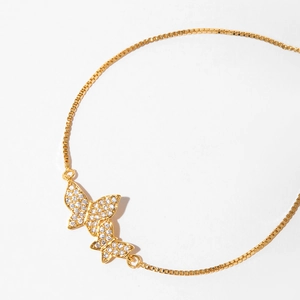 Detail of adjustable gold bracelet featuring two butterfly charms with micro-pave crystals