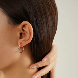 Close-up of polished silver titanium steel hoop earring worn on model's ear