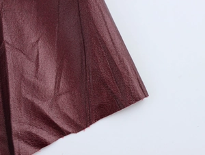 Dettaglio macro della texture in finta pelle rosso scuro con pieghe e bordi a taglio vivo