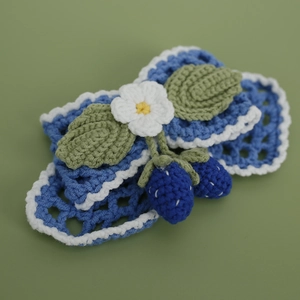 Handmade crochet hair clip with blue flowers and berries on a soft green background