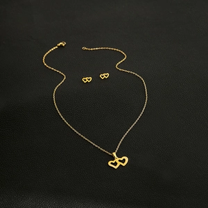 Detailed close-up of golden double heart pendant necklace and matching stud earrings set
