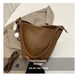 Detailed shot of brown lychee grain leather bucket bag with mini baseball charm and straps