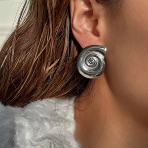 Detailed close-up of a silver spiral shell earring featuring a polished mirror finish