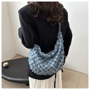 Detail of blue denim crossbody bag featuring checkered weave and frayed fringe edges