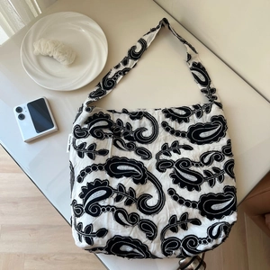 Detail of white cotton canvas shoulder bag with dense black paisley floral embroidery