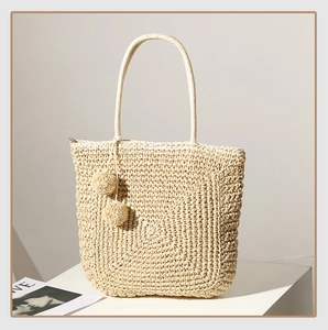 Detail view of woven straw tote bag texture and soft beige pompom decorative tassels