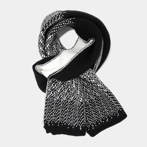 Detail of black and white knitted scarf featuring dot pattern and ribbed edge finish