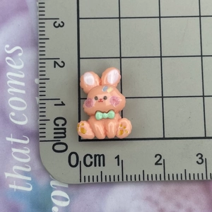 Close-up of pink resin rabbit charm with green bow and glitter, sized 2.5cm on scale