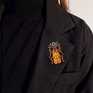 Dettaglio di una spilla a scarabeo vintage con cristalli colorati su un bavero nero