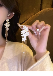 Macro detail of long gold tassel earrings with 3D white flower and sparkling crystal charms