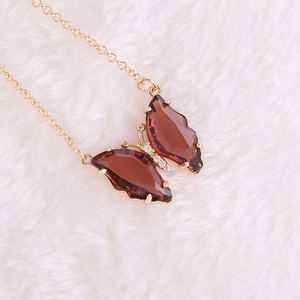 Detail view of a gold butterfly pendant with amber stones on white plush background