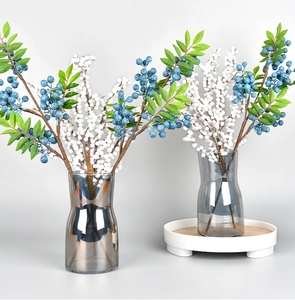 Close-up of blue and white artificial berries in grey glass vases for holiday decor