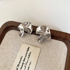 Macro view of silver irregular pleated floral earrings on a wooden display tray