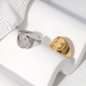 Detail of gold and silver smiley face open rings displayed on a white wave stand