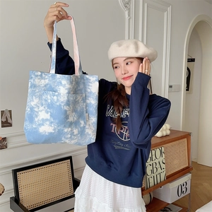 Dettaglio della borsa tote in tela tie-dye blu e bianca con tasca frontale e etichetta in tessuto