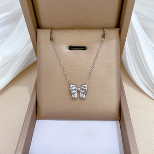Elegant silver bow pendant necklace displayed on a jewelry box with silk fabric