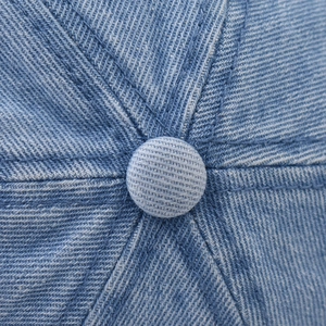 Detail of the stitched crown and top button on a washed blue denim baseball cap
