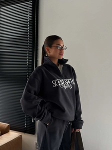 Close-up of letter embroidery on dark grey half-zip sweatshirt with light shadow effect