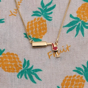 Gold-plated wine bottle and glass pendant necklace with red heart detail on a pineapple print