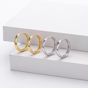 Close-up of gold and silver minimalist hoop earrings on white geometric stands