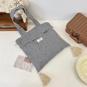 Close-up of black gingham canvas tote bag featuring cream tassels and a fabric label