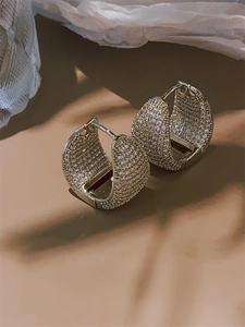 Macro shot of silver paved cubic zirconia C-shaped hoop earrings on elegant textured surface