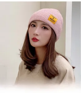 Detailed view of pink ribbed knit beanie featuring a yellow square logo patch and soft texture