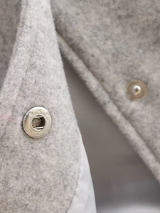 Vue détaillée de la texture du lainage gris clair et du bouton pression en métal