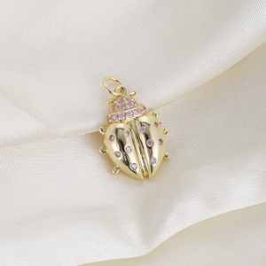 Macro view of gold ladybug charm with pink gemstones on beige silk fabric