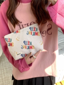 Corduroy makeup bag with smile print and zipper closure held by model in casual style