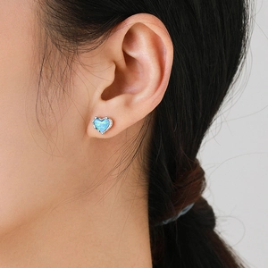 Elegant heart-shaped blue opal stud earrings in silver, worn by a model in a close-up view