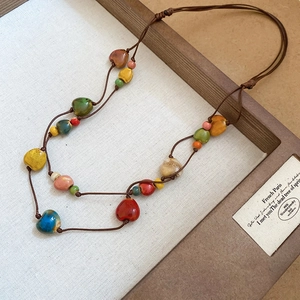 Dettaglio collana bohémien con perle di ceramica a cuore e conchiglia su vassoio
