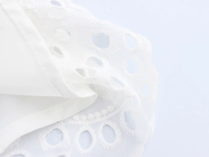 Dettaglio di un elegante abito bianco senza maniche con ricami traforati e trama in pizzo