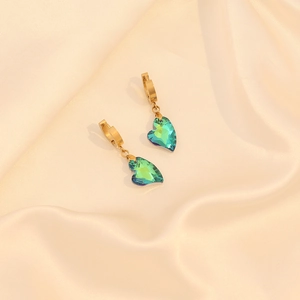 Détail de boucles d'oreilles dorées avec cristal de cœur sur soie beige