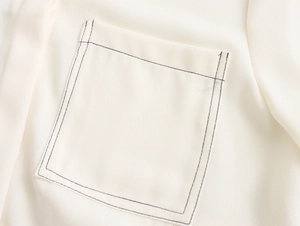 Detailed view of an off-white blouse pocket featuring contrasting black stitching lines