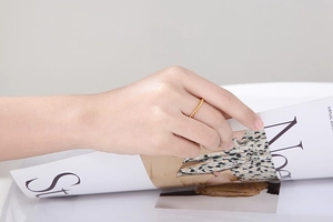 Detail of a thin twisted gold ring worn by a model while flipping through a magazine