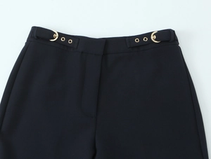 Detail of black crepe trousers featuring adjustable side buckles with gold metal hardware